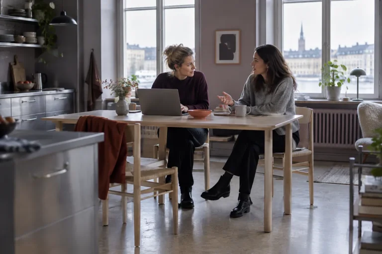 Två personer sitter vid ett köksbord med en laptop och pratar